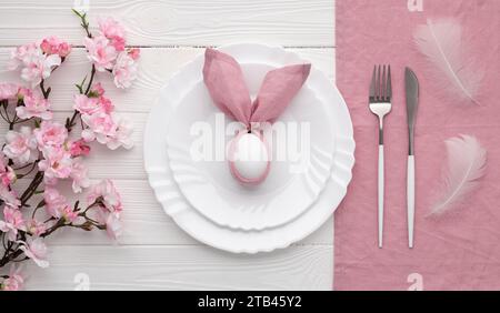 Festive Easter table setting with bunny made of pink linen napkin and egg. Top view. Happy Easter holiday concept for restaurant menu. Empty plate and Stock Photo