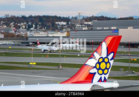 Vertical stabiliser of an Airbus of the Swiss holiday airline Edelweiss Air, behind it two aircraft of Swiss International Air Lines on the runway Stock Photo