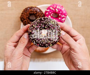 High angle view of chocolate donut with sprinkles in male hands. Stock Photo