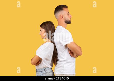 Sad angry millennial european wife and husband in white t-shirts back to back, ignoring after quarrel Stock Photo