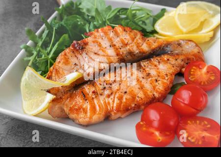 Grilled Butterfly Salmon Steak with cherry tomatoes and arugula salad on a white square plate. Close-up. Stock Photo