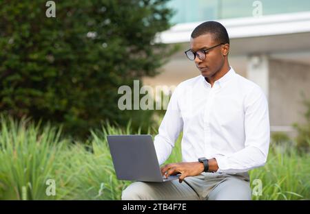 Professional black businessman in glasses using laptop while seated outside Stock Photo