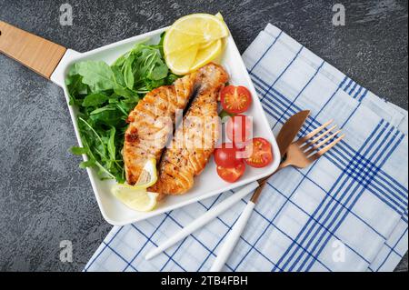 Grilled Butterfly Salmon Steak with cherry tomatoes and arugula salad on a white square plate. Close-up. Top view, flat lay, copy space. Stock Photo