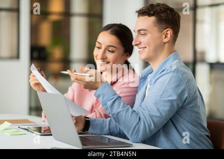 Positive millennial middle eastern woman and caucasian guy manager work with documents Stock Photo