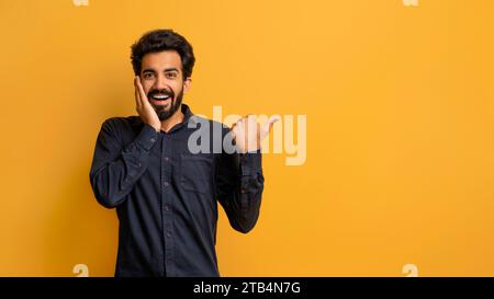 Amazing Offer. Excited Indian Guy Touching Face And Pointing At Copy Space Stock Photo