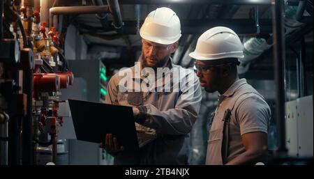 Multiethnic team of technician specialists work together on factory using laptop and tablet computer. Professional engineers discuss industrial manufacturing technology. Concept of heavy industry. Stock Photo