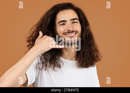 man with curly hair gesturing call me playfully, beige background Stock Photo