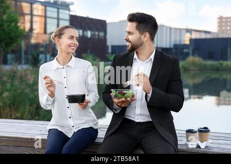 Smiling business people eating from lunch boxes outdoors Stock Photo