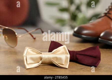 Stylish color bow ties, sunglasses and shoes on wooden table Stock Photo