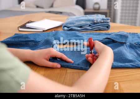 Woman cutting jeans with scissors at wooden table, closeup Stock Photo