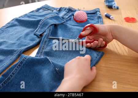 Woman cutting jeans with scissors at wooden table, closeup Stock Photo