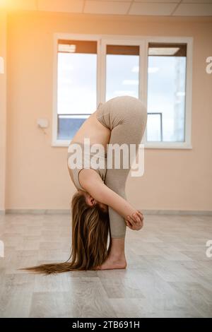 young woman doing yoga in the gym a girl with a long braid and in a beige tracksuit stands in a stork pose on a pink carpet a woman performs 2tb691h
