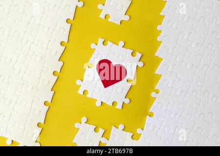 Puzzle pieces that make up a heart on the yellow background. The concept of a complementary relationship, solving love problems together. Stock Photo