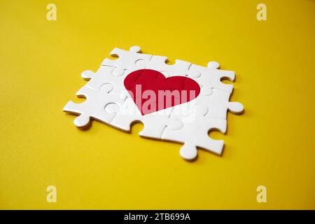 Puzzle pieces that make up a heart on the yellow background. The concept of a complementary relationship, solving love problems together. Stock Photo