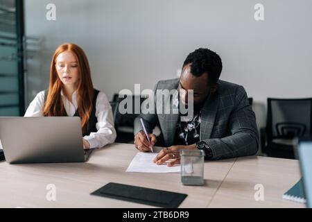 Portrait of serious African-American in formal suit putting signature on new contract to starting projects in conference room. Stock Photo