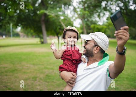 Beautiful Young indian father wearing hat and sunglasses dancing with his baby girl in the park or garden. Stock Photo