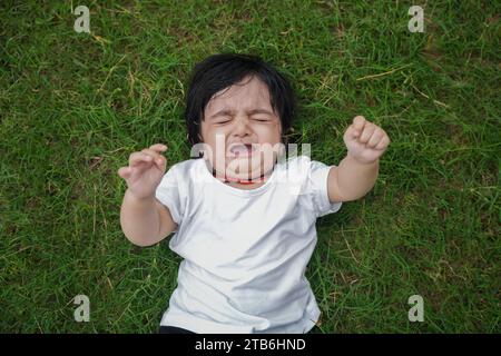 Cute indian boy lying in garden crying. Stock Photo