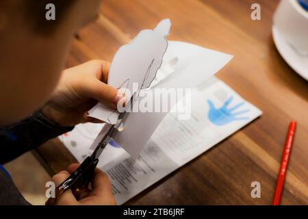 A child cuts paper with scissors, carves figures of knights while sitting at a table Stock Photo