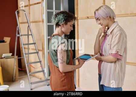 Girls using tablet pc to choose color for design of new apartment during repair Stock Photo