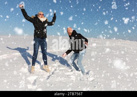 A young couple, consisting of a woman and a man, jump in the air in the snow and have fun together Stock Photo