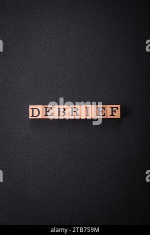 The inscription debrief in wooden cubes on a dark concrete background. Can be used as part of your composition Stock Photo