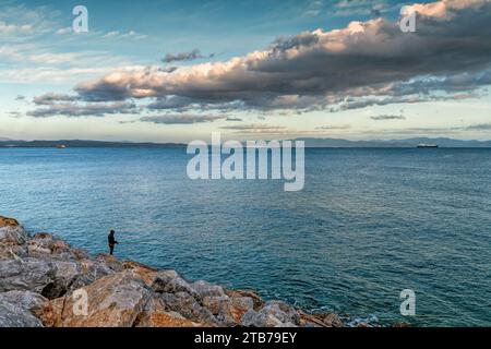 Piombino, Italy - 11 November, 2023: lone fisherman fishing off the harbor jetty at Piombino harbor at sunset Stock Photo