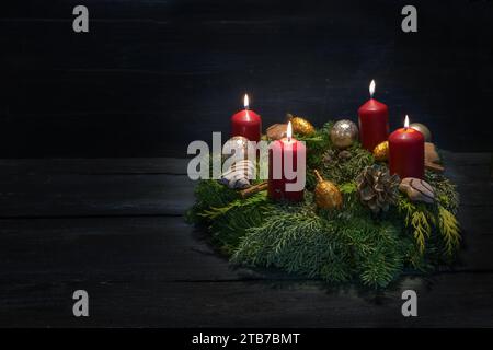 Light in the dark on fourth advent, natural green wreath with red candles, four are burning, Christmas decoration and cookies, dark wooden background, Stock Photo