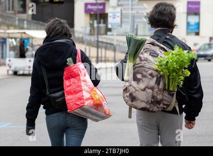 Annonay (south-eastern France): atmosphere on a winter market day. Young couple with shopping bags and vegetables sticking out of a backpack, leeks an Stock Photo