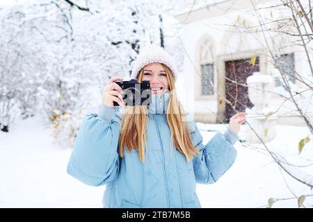 Blond smiling girl photographed on an old vintage camera in winter forest Stock Photo