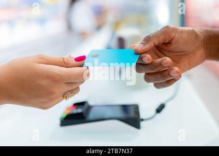 Cropped hands of anonymous female customer giving blue credit card for payment to cashier at checkout in pharmacy store in blurred background Stock Photo