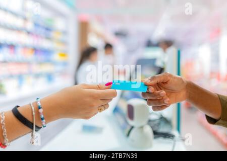 Cropped hands of anonymous female customer giving blue credit card for payment to cashier at checkout in pharmacy store in blurred background Stock Photo