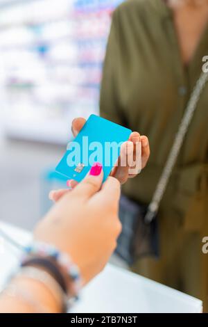 Cropped hands of anonymous female customer giving blue credit card for payment to cashier at checkout in pharmacy store Stock Photo