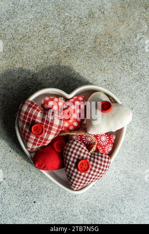 From above heart shaped bowl filled with assorted handmade fabric hearts on a textured concrete background during Valentine's day celebrations Stock Photo