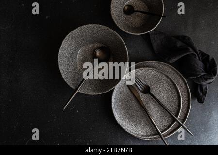 An aesthetic arrangement of dark stoneware dishes with a rustic charm, set on a dark textured background, highlighting minimalistic tableware design. Stock Photo