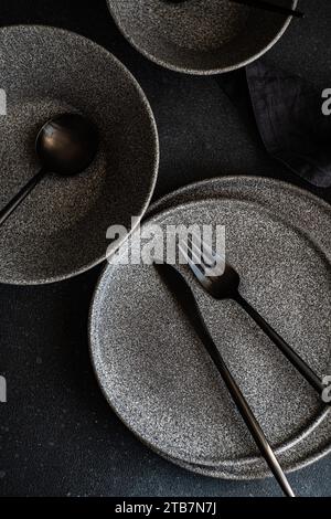 An artistic shot of a modern tableware set, including plates and utensils, arranged on a dark, textured surface. Stock Photo