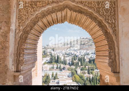 Beautiful view of townscape with residential buildings and trees on mountain against cloudy blue sky seen through arched window of famous Alhambra pal Stock Photo