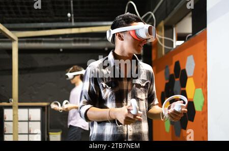 Side view of young excited man is engaged in a virtual reality game wearing a VR headset and using controllers Stock Photo