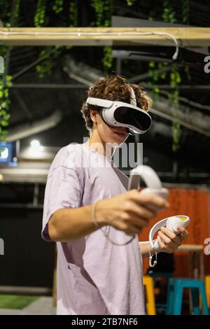 Side view of young excited man is engaged in a virtual reality game wearing a VR headset and using controllers Stock Photo