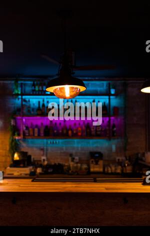A close-up of a lit pendant lamp with a glowing filament bulb, illuminating a bar shelf with bottles in the background Stock Photo