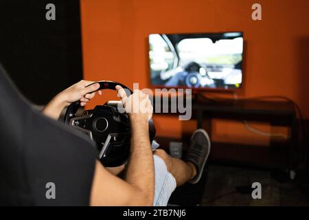A person is engaged in playing a racing video game using a steering wheel controller in a home setting with a television in the background. Stock Photo