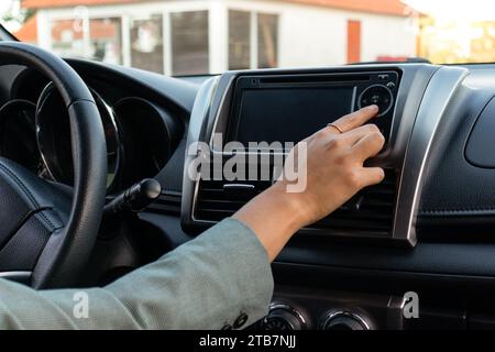 Cropped hand of anonymous businesswoman using infotainment on dashboard by steering wheel inside luxury automobile during daytime Stock Photo