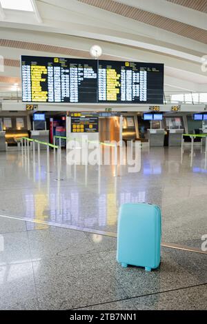 Blue trolley bag on tiled floor with arrival departure board in background inside empty airport terminal Stock Photo