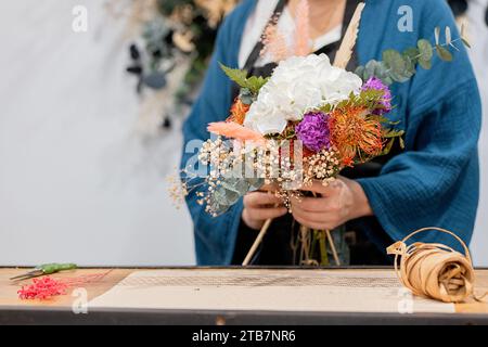 Unrecognizable person crafting a bouquet, arranging flowers on a wooden table, with twine and scissors nearby Stock Photo