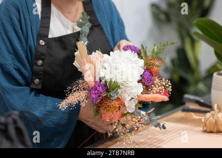 Unrecognizable person crafting a bouquet, arranging flowers on a wooden table, with twine and scissors nearby Stock Photo