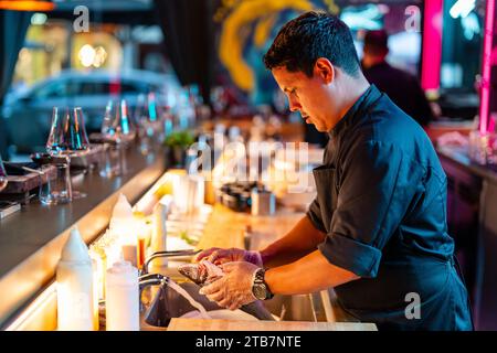 Side view of confident male chef wearing gloves with concentration washing dead fish in sink at counter of modern sushi bar Stock Photo