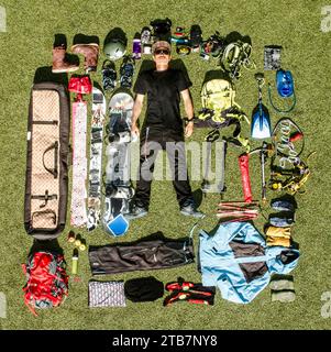 Overhead full body of young man dressed in black casuals lying on grassy land surrounded with various hiking equipment and tools Stock Photo