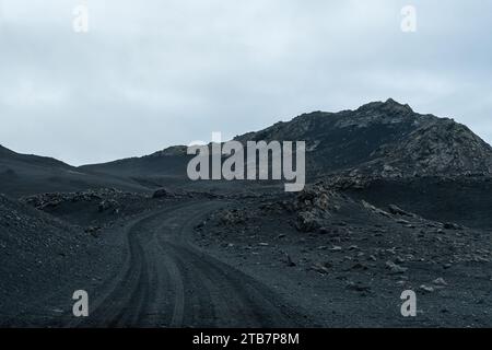 A desolate gravel road meanders through the stark and rugged landscape of the Icelandic Highlands under a gloomy sky Stock Photo