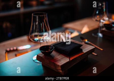 An intimate setting of a sushi restaurant with a wooden table, elegant glassware, and a stone plate awaiting delicious cuisine. Stock Photo