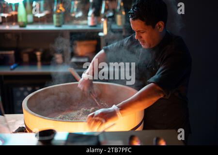 A focused sushi chef prepares fresh rice for sushi dishes in the ambient setting of a sushi restaurant. Stock Photo