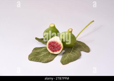 A composition of ripe green figs, one sliced in half, with a detailed leaf on a clean white surface. Stock Photo